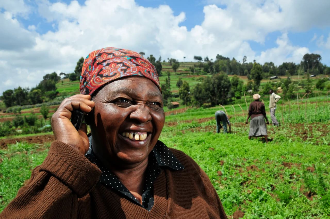 A smiling farmer in a headscarf talking on a mobile phone in a green field